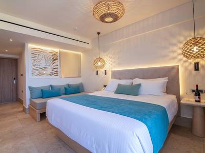 Modern hotel room with large bed, turquoise accents, and warm lighting.