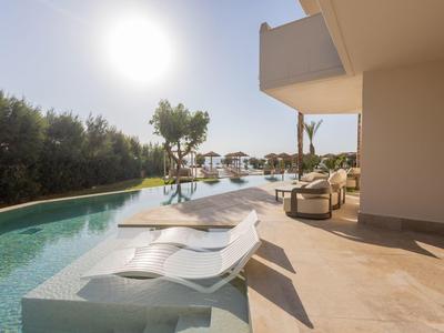 Pool area with lounge chairs in the water and sunshine beside a modern terrace.