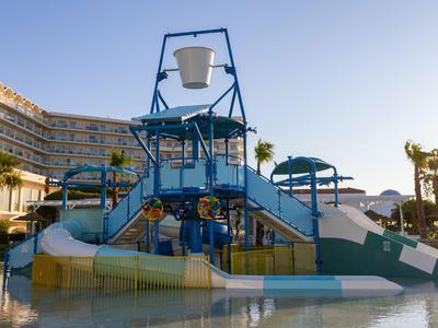 Wasserpark mit blauen Rutschen und Planschbecken neben Hotelgebäude bei sonnigem Himmel.