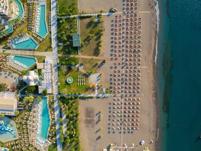 Luftaufnahme eines Strandes mit Reihen von Sonnenschirmen neben Hotelanlagen und klarem Meer.