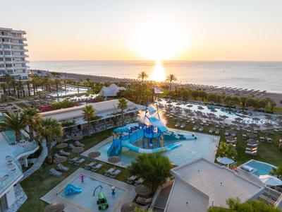 Hotelpool mit Wasserrutschen und Liegestühlen am Meer bei Sonnenuntergang.