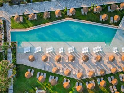 Luftaufnahme eines trapezförmigen Pools mit Sonnenliegen und Sonnenschirmen in einem Hotelgarten.