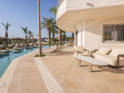 Moderne Hotelterrasse mit bequemen Liegestühlen und Blick auf den Pool und Palmen.