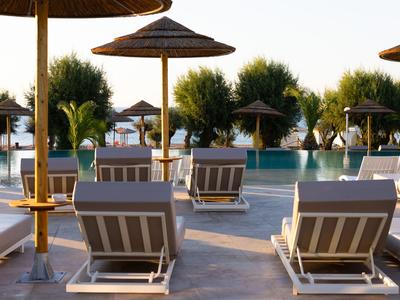 Hotelpool mit Liegestühlen und Sonnenschirmen, umgeben von Bäumen im Sonnenlicht.