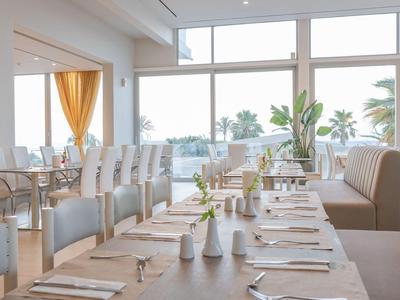 Helles Restaurant mit eingedeckten Tischen und Blick auf Palmen im Hintergrund.