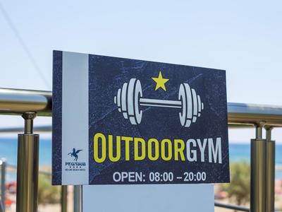 Schild mit Aufschrift 'Outdoor Gym' und Öffnungszeiten vor klarem Himmel.
