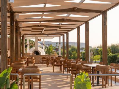 Offene Hotelterrasse mit Holzmöbeln und weißem Sonnendach, umgeben von Pflanzen.