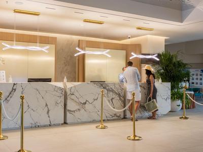 Moderner Hotellobby mit Marmorrezeption und zwei Gästen im Gespräch.