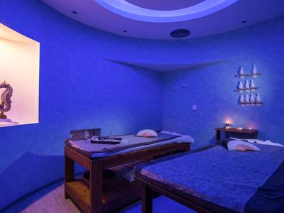 Ruhiger Wellnessraum mit zwei Massageliegen, blauem Licht und dekorativen Wandregalen.