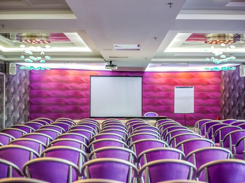 Conference room with rows of purple chairs, a screen, and a flipchart for meetings.