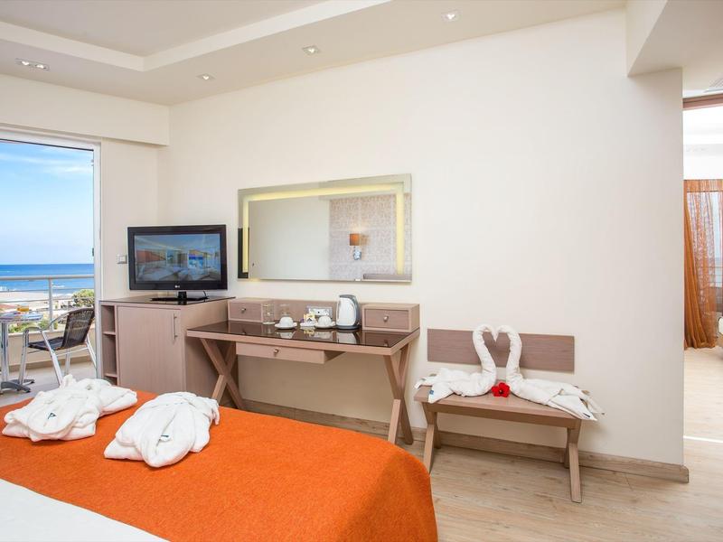 Bright hotel room with sea view, orange bedspread, TV, desk, and balcony.