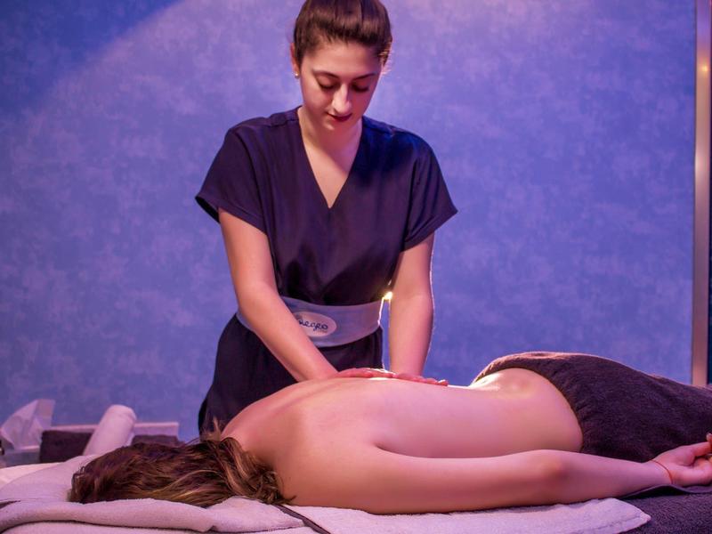 Woman receiving back massage from therapist in calm, blue-lit spa room.