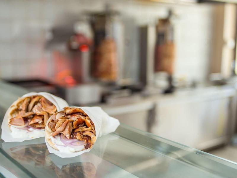 Two doner wraps with meat and vegetables on a glass countertop in a fast food setting.
