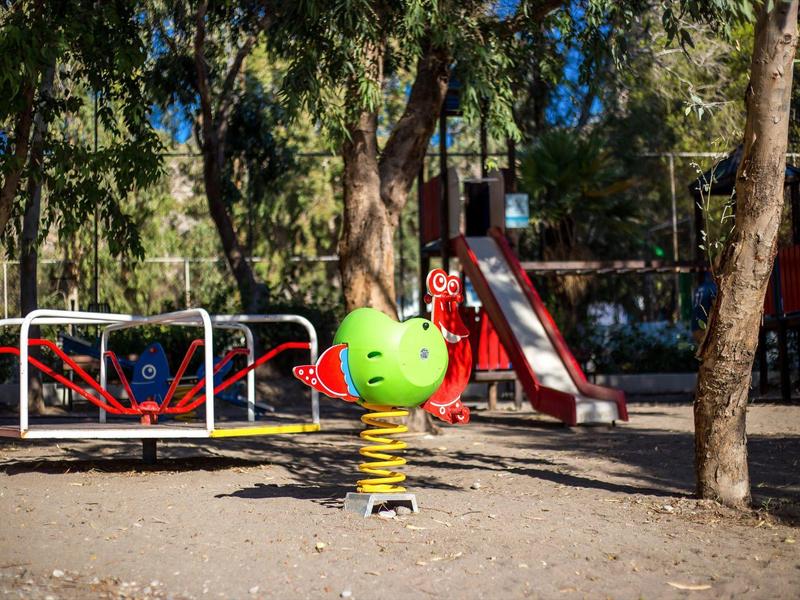 Playground with green spring rider, carousel, and red slide among trees.