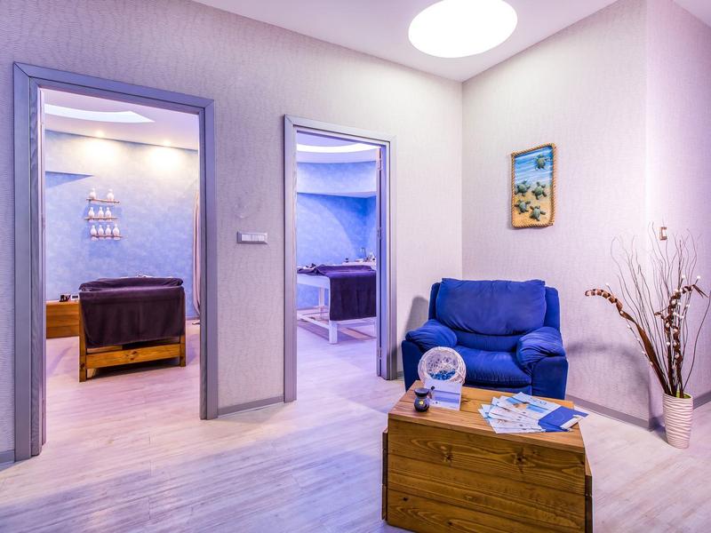 Modern furnished hotel waiting area with sofa, wooden table, and view into two rooms.