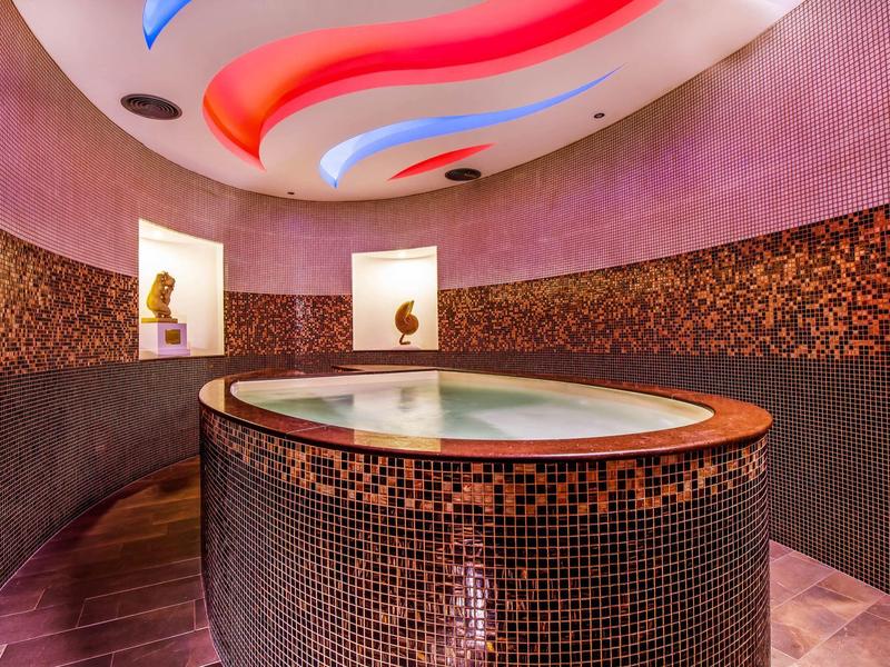 Modern spa with a round pool and colorful illuminated ceiling design.
