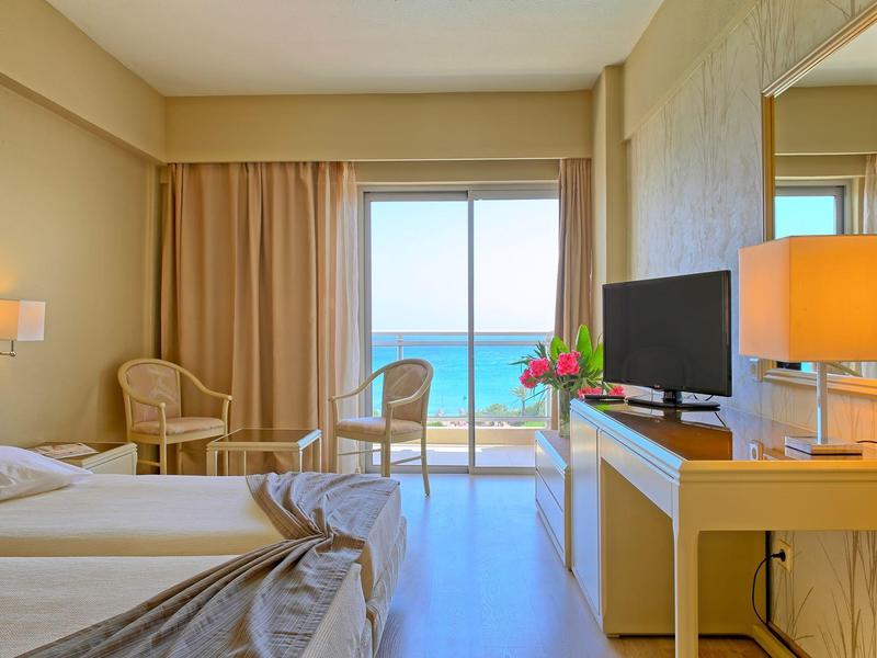 Brightly furnished hotel room with two beds and sea view through large windows.