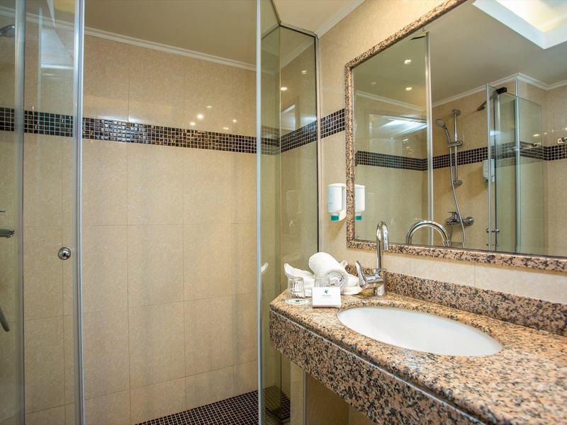 Bright hotel shower with glass enclosure and sink on marble countertop.
