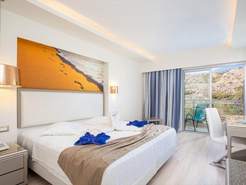 Bright, modern hotel room with double bed, balcony, and rocky landscape view.