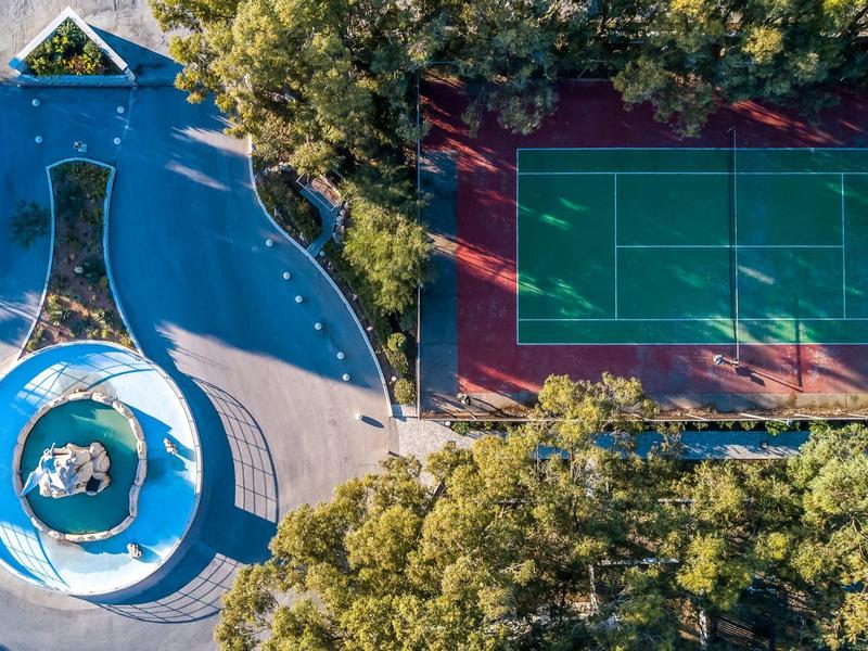 Aerial view of a tennis court next to a circular terrace with a fountain.