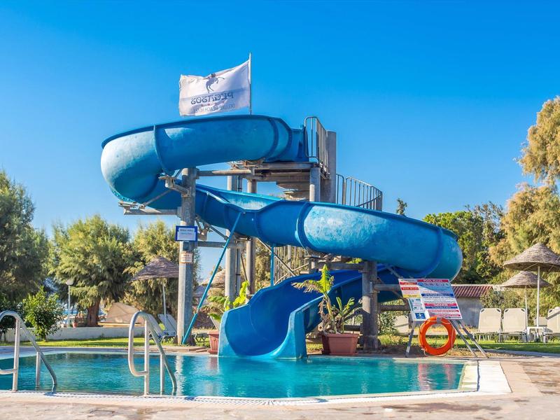 Water slide at an outdoor pool with sun umbrellas and trees in the background.