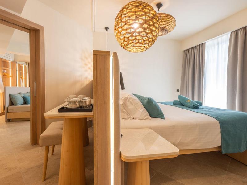 Bright hotel room with double bed, blue pillows and curtains, wooden and stone elements.