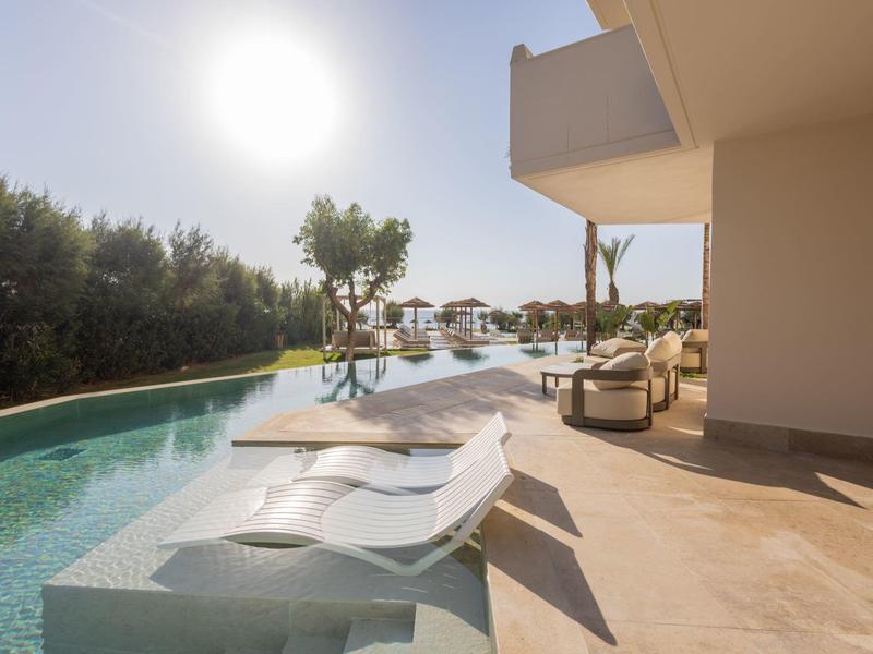 Pool area with lounge chairs in the water and sunshine beside a modern terrace.