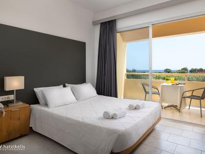 Moderní hotelový pokoj s manželskou postelí, nočními lampami a balkonem s posezením a výhledem do zeleně.