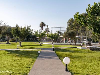 Weg durch grünen Park mit Bäumen, Lampen und blauem Himmel.