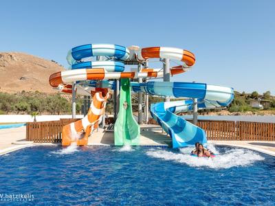 Kolorowe zjeżdżalnie wodne nad basenem z górami w tle pod słonecznym niebem.