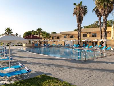 Basen hotelowy z niebieskimi leżakami i palmami o zachodzie słońca.