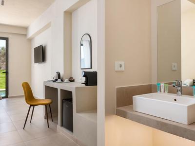 Moderní hotelový pokoj s psacím stolem, televizí, žlutou židlí a umyvadlem v koupelně.