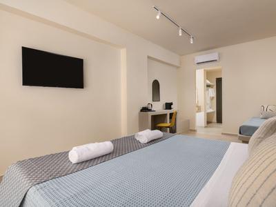 Pokoj s dvěma postelemi, televizí na zdi a pracovním koutem se židlí v minimalistickém designu.