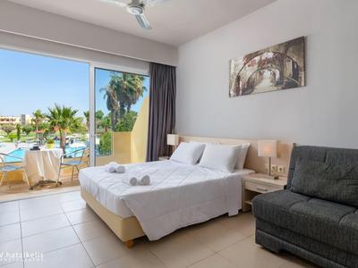 Světý hotelový pokoj s manželskou postelí, balkonem, výhledem na bazén, moderním zařízením a pohovkou.