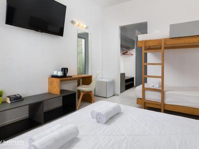 Moderní hotelový pokoj s patrovou postelí, psacím stolem, televizí a čistými bílými ručníky.