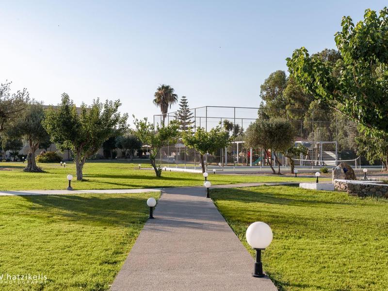 Přímá chodníková cesta vede udržovanou zelenou zahradou s stromy a lampami.