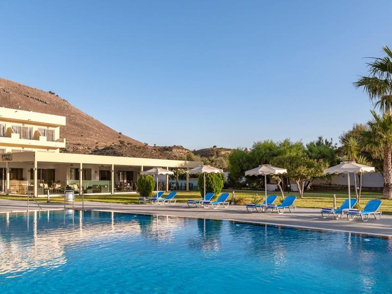 Hotelový bazén s lehátky a palmami pod jasnou oblohou.