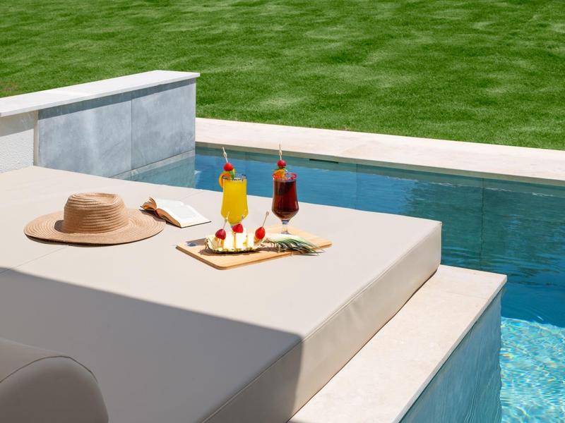 Sluneční terasa s podnosem na nápoje vedle hladkého bazénu a zeleného trávníku.