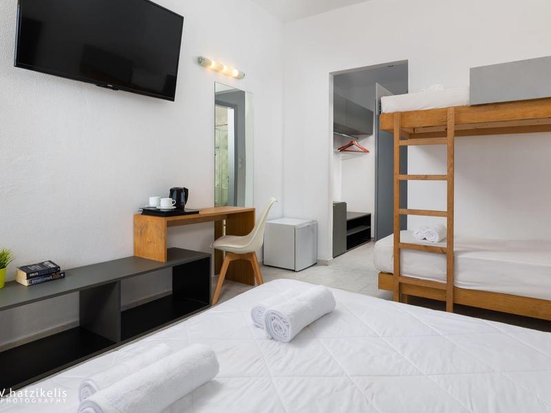 Moderní hotelový pokoj s patrovou postelí, psacím stolem, televizí a čistými bílými ručníky.