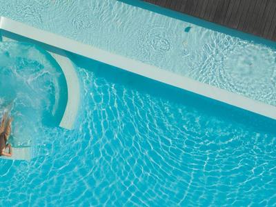 Person entspannt sich am Rand eines sauberen, blauen Hotelpools auf einer Terrasse.