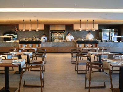 Modernes Restaurant mit Holztischen, Stühlen und offener Küche im Hintergrund.