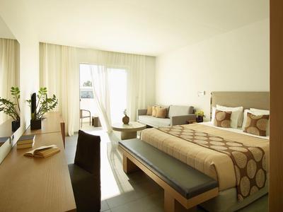 Helles Schlafzimmer mit Doppelbett, Schreibtisch, Sofa und Balkon, beige und braune Farbtöne.