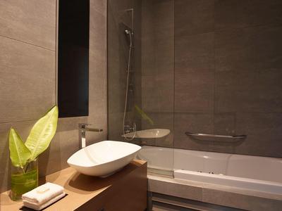 Modernes Badezimmer mit grauen Fliesen, Holzwaschtisch, weißem Waschbecken und Badewanne.