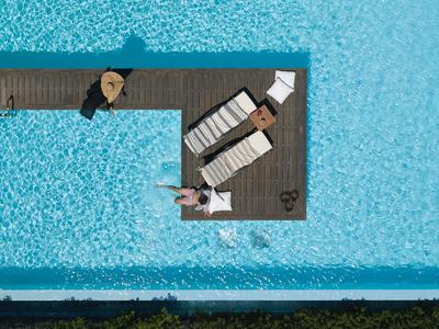 Widok z góry na basen z dwoma leżakami i osobą na drewnianym pomoście.