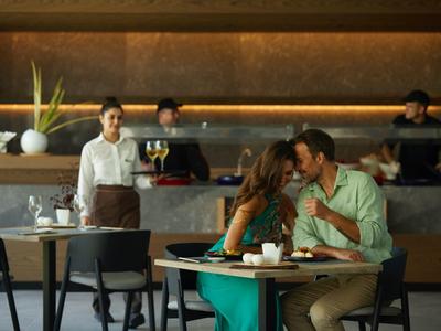 Paar genießt Kaffee an einem Tisch in einem modernen Café mit Barista im Hintergrund.