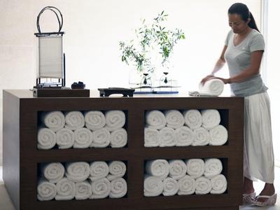 Eine Frau ordnet in einem Hotel Wellnessbereich frische Handtücher auf einem Holzwagen.