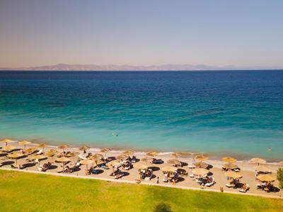 Strand mit Sonnenschirmen und Liegestühlen neben blauem Meer und klarem Himmel.