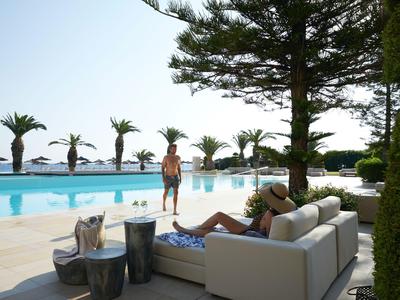 Ludzie odpoczywają przy basenie obok palm w słonecznym, luksusowym ośrodku.