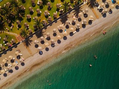 Luftaufnahme eines Strandes mit Sonnenschirmen, Palmen und klarem, grünem Wasser.