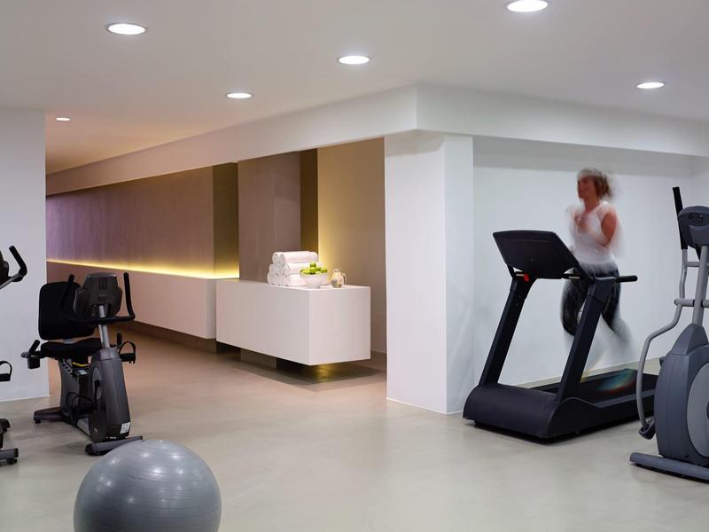 Moderner heller Fitnessraum mit Laufband, Fahrradergometer und Gymnastikball auf hellem Boden.